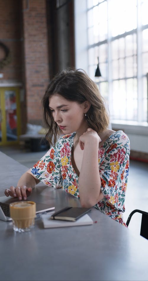 喝她的咖啡时使用笔记本电脑的花衬衫的女人 · 免费素材视频