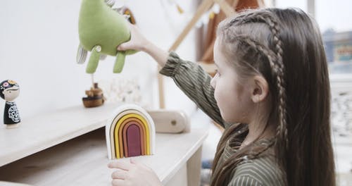 一个搁在恐龙毛绒玩具上玩木制玩具的女孩 · 免费素材视频