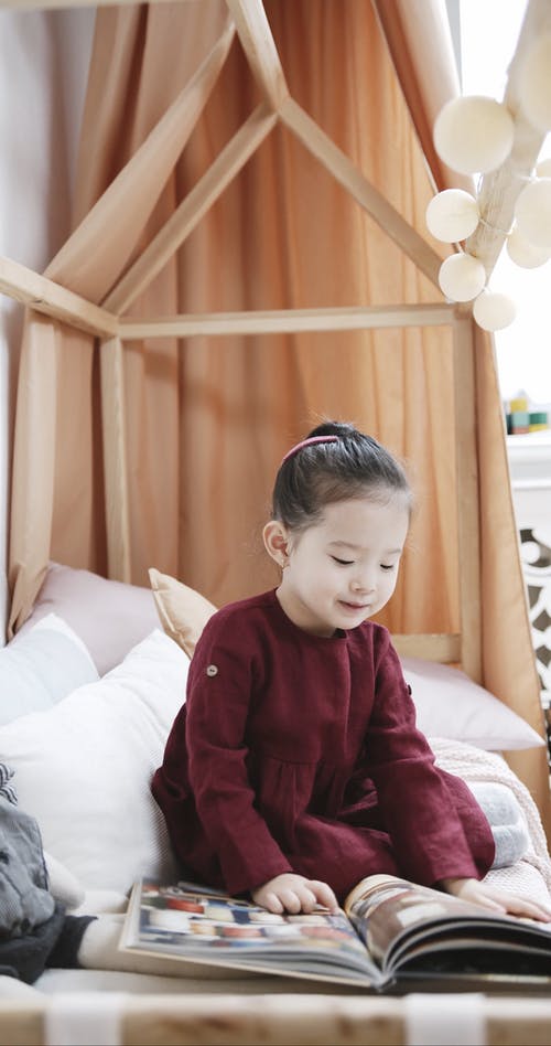 小女孩坐在床上看书中的图片 · 免费素材视频