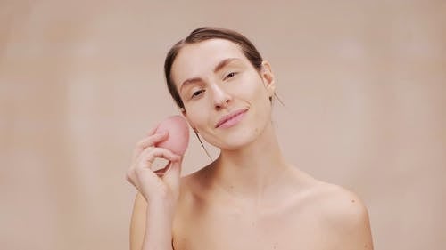 女人在她的脸上使用粉红色海绵 · 免费素材视频