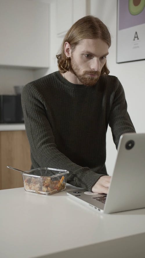 一个人在办公室厨房的笔记本电脑上工作时吃早餐 · 免费素材视频