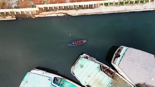 一艘小木船经过停靠在海湾的大型渔船 · 免费素材视频