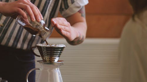 一名男子将咖啡粉倒在锡杯过滤器上制成热煮咖啡 · 免费素材视频