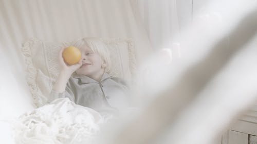 一个躺在吊床上的男孩玩捉住并扔出橙色水果 · 免费素材视频