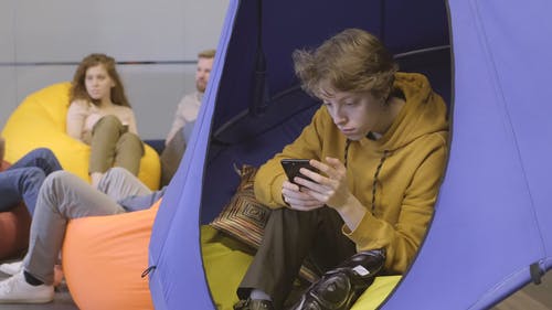 一个年轻人坐在摇摆的帐篷上时使用他的手机 · 免费素材视频