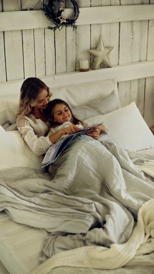 母亲和女儿在一起躺在床上看着一本杂志 · 免费素材视频