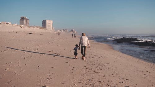 一位母亲和儿子在海滩岸上手拉手奔跑 · 免费素材视频