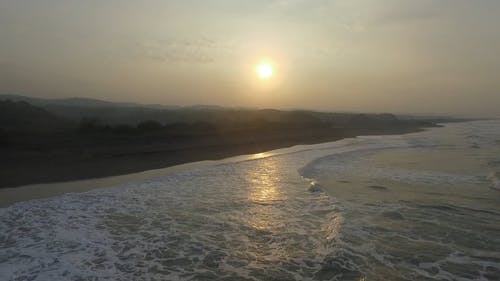 海浪冲向岸，背景为日落 · 免费素材视频