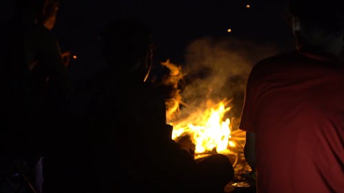 在黑暗的夜晚坐在篝火旁的人为热和光 · 免费素材视频