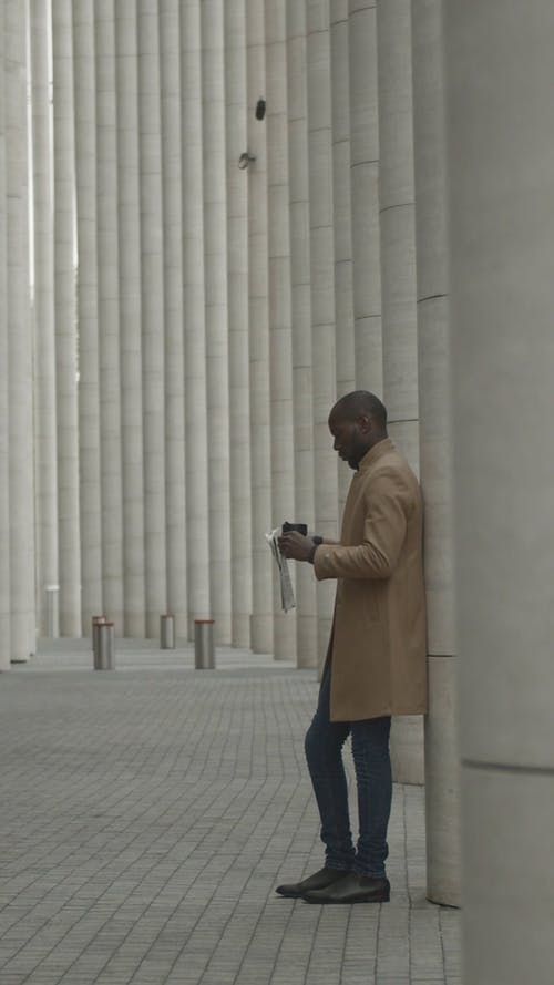 一个男人用一杯饮料和报纸在混凝土支柱上倾斜的手上 · 免费素材视频