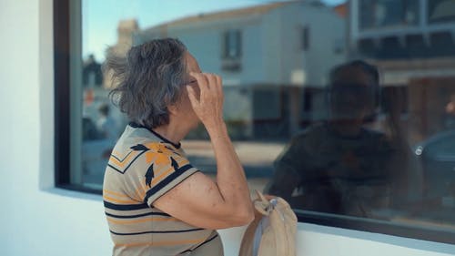 一名老妇在玻璃窗前看着自己 · 免费素材视频