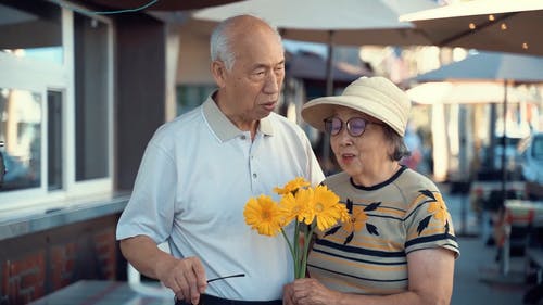 老年夫妇站在街边拿着黄色的花 · 免费素材视频