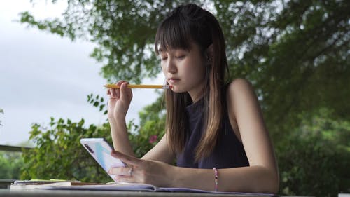 一个女人在使用她的智能手机时学习和写作 · 免费素材视频