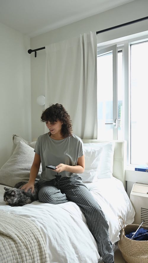 一个女人坐在她的猫的床上 · 免费素材视频