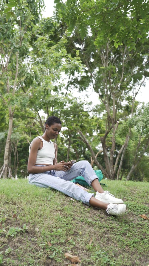 一个女人坐在草地上，一边使用她的智能手机 · 免费素材视频
