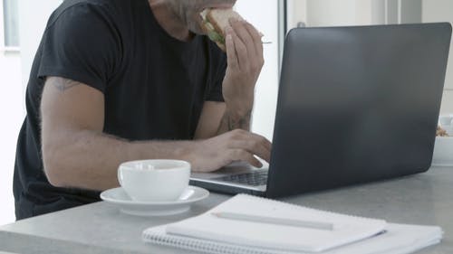 一个人在用笔记本电脑工作时吃三明治 · 免费素材视频