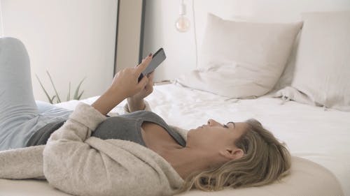 使用她的手机躺在床上的女人 · 免费素材视频