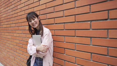 一个女人微笑着站在一堵砖墙附近 · 免费素材视频