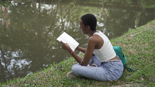 一个女人坐在草地上，一边读她的笔记 · 免费素材视频
