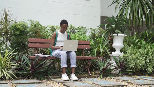 一个女人坐在长椅上同时使用她的笔记本电脑，然后由她的朋友打招呼 · 免费素材视频