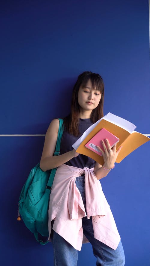 一个女人站在蓝色的墙壁附近读她的笔记 · 免费素材视频