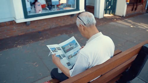 老人坐在长椅上看报纸 · 免费素材视频