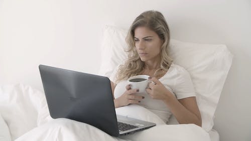 一个女人喝咖啡，在床上使用她的笔记本电脑 · 免费素材视频