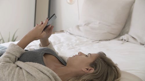 使用她的智能手机时躺在床上的女人 · 免费素材视频